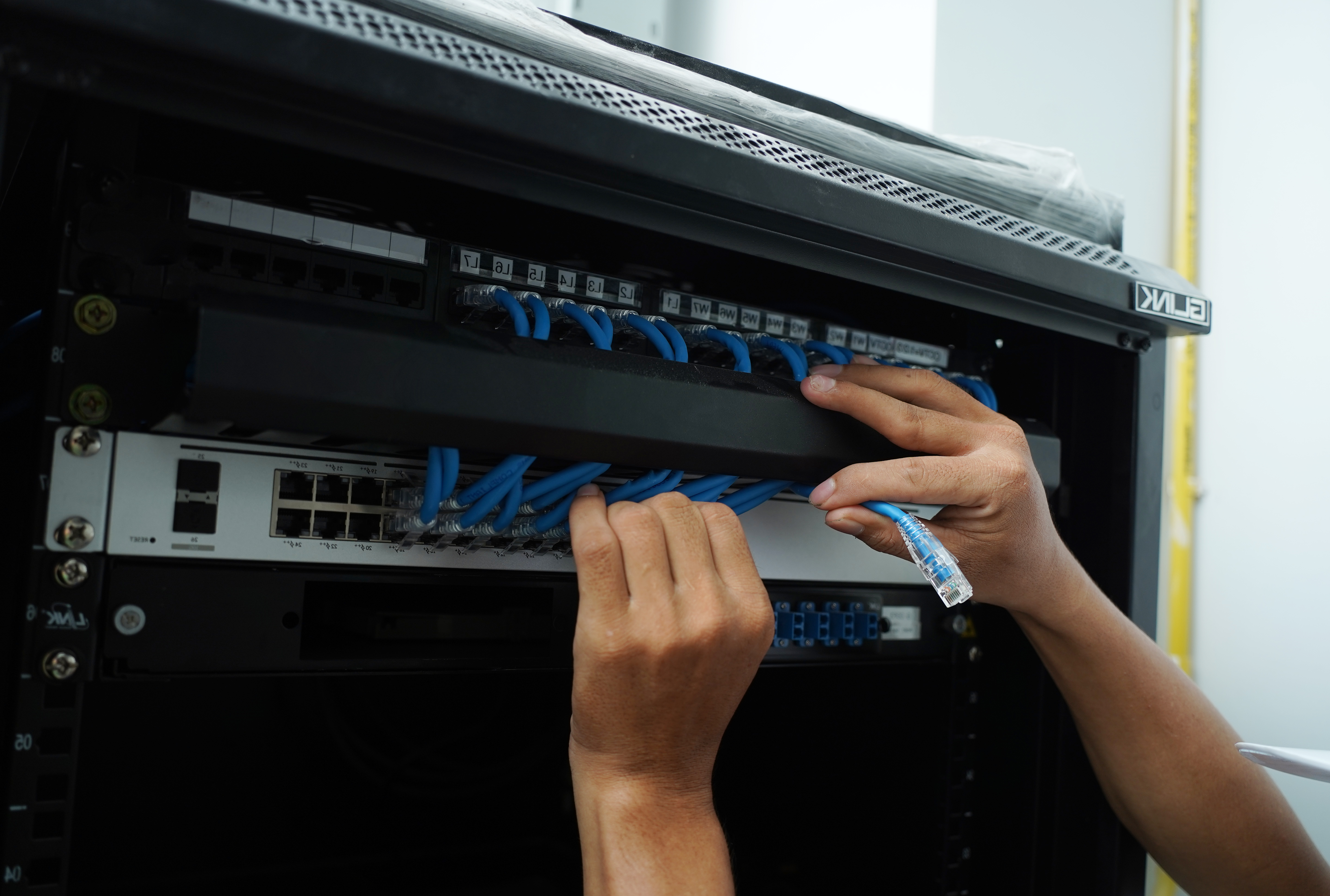 A maintenance technician works in a server room with a fiber optic hub.