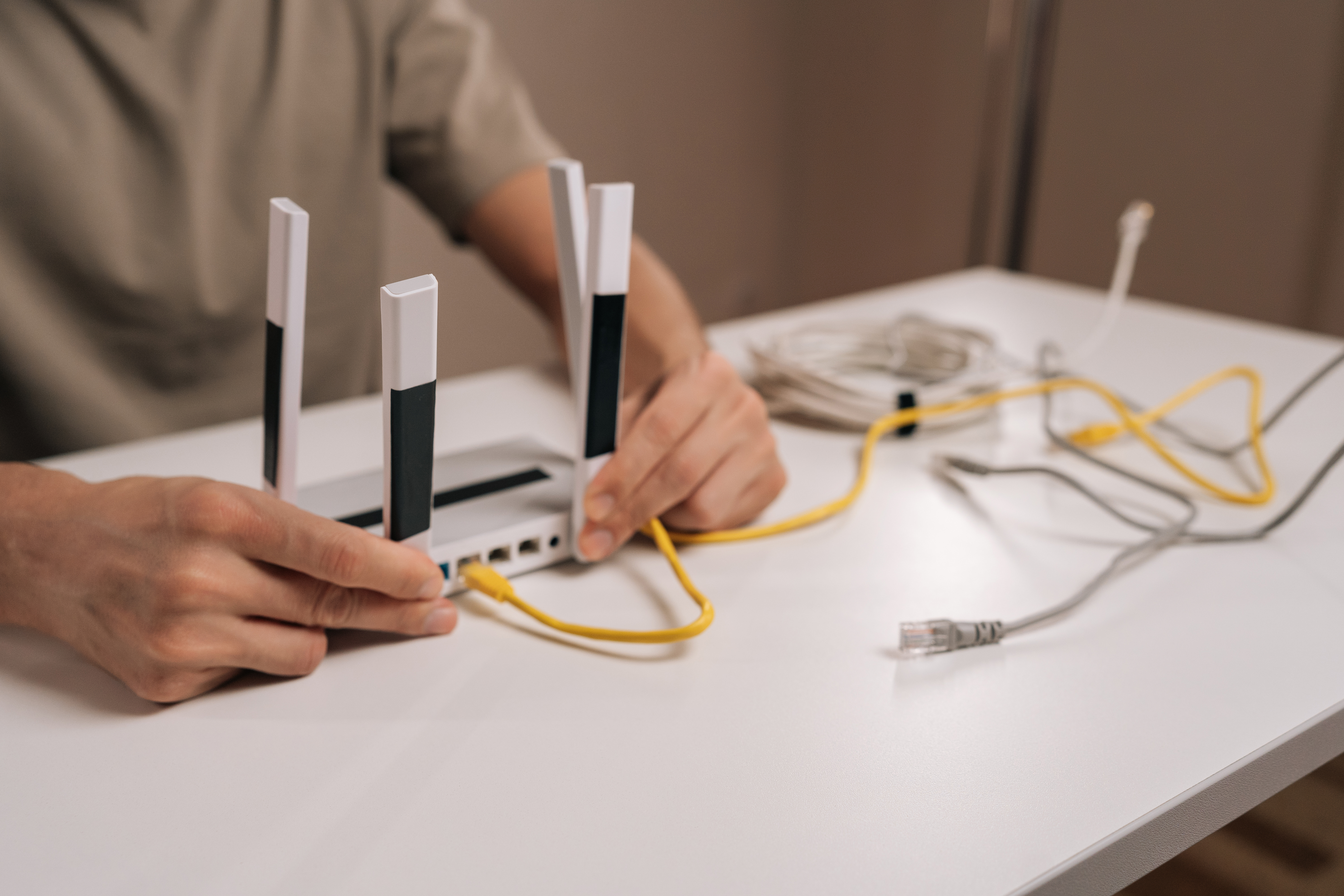 Close-up of technician hands connecting yellow ethernet cable into the port of a modern white wireless router with multiple antennas, symbolizing network setup and internet connectivity.