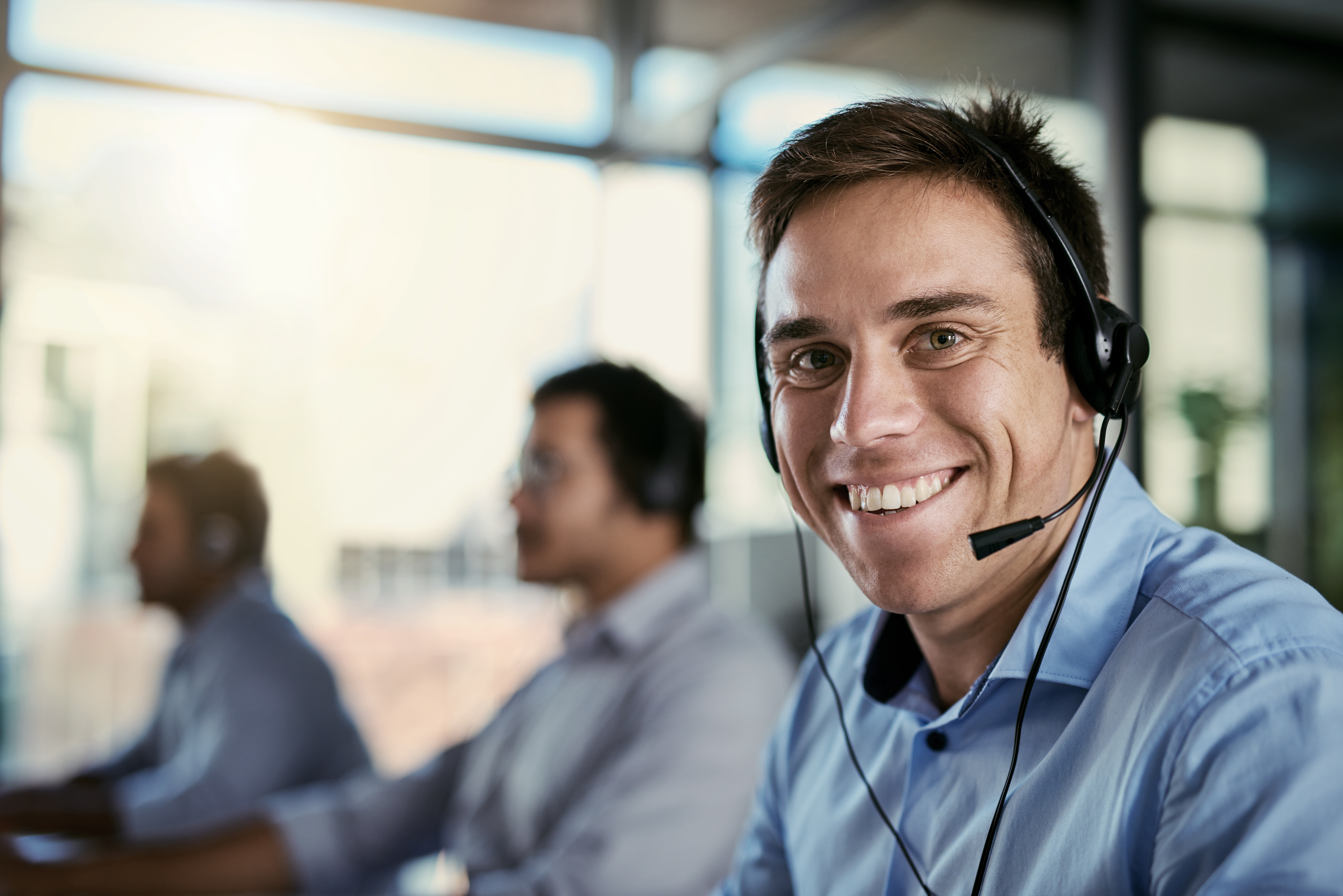 Portrait of a call centre agent working in an office with his colleagues in the background