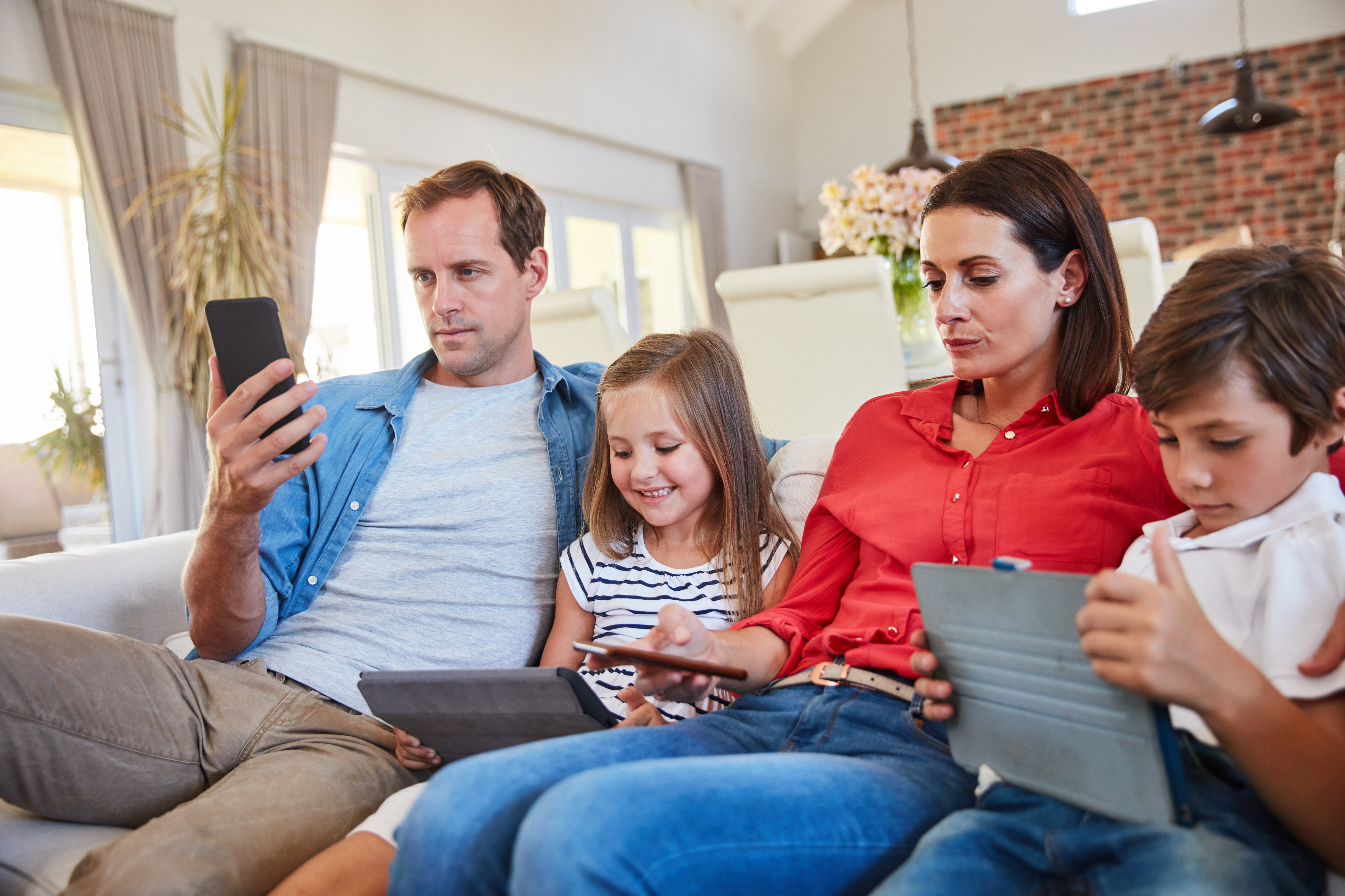 Shot of a young family sitting together on their living room sofa distracted by various media and devices